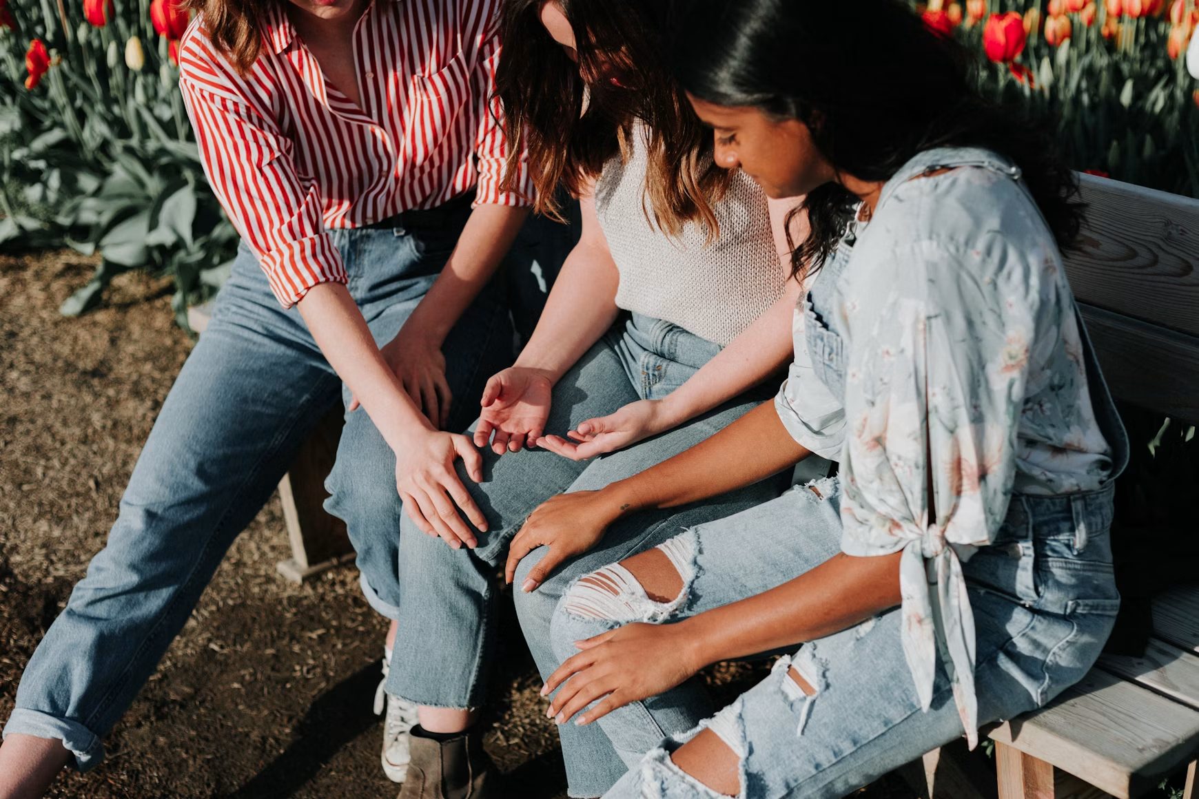 Three friends sitting together on a bench beside a field of tulips, in warm evening light.