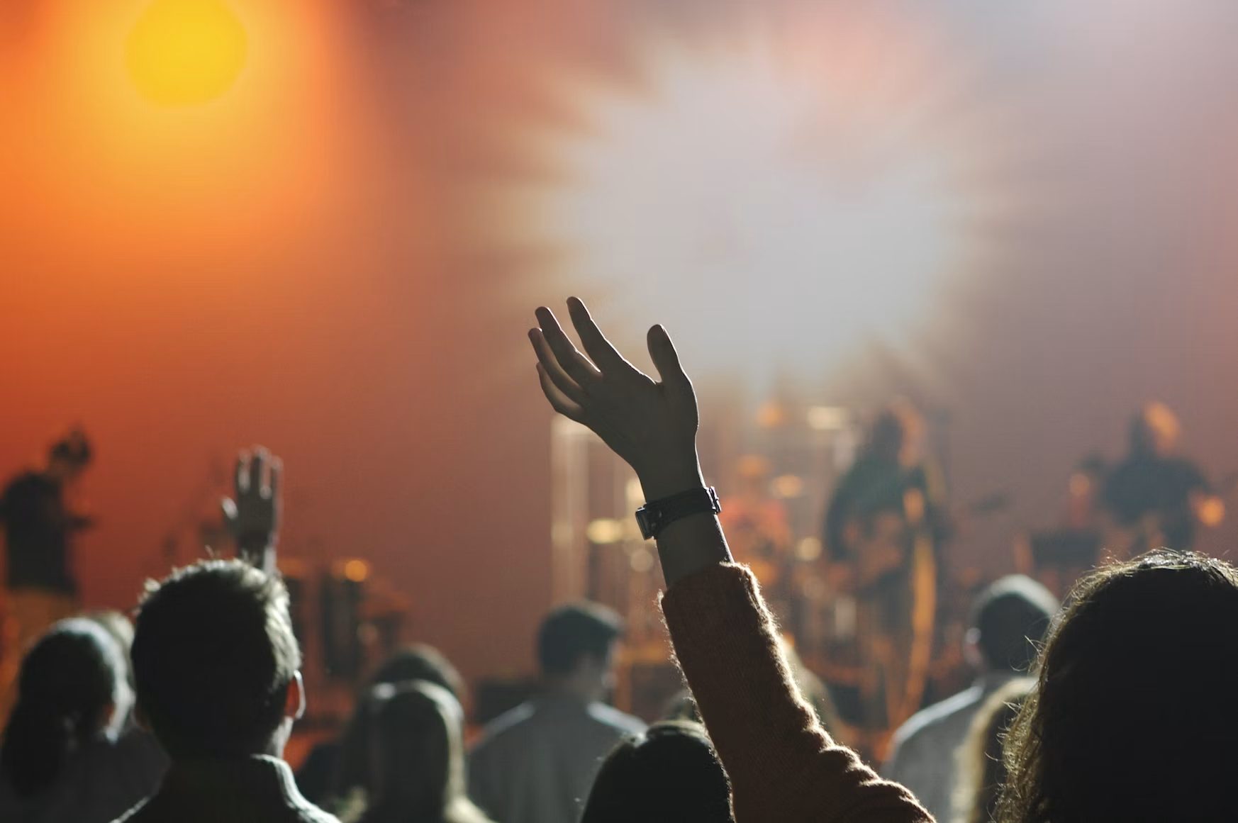 Hands raised in worship under warm stage light.